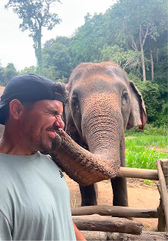 Adrián sonriendo junto a un elefante que le acerca la trompa a la cara